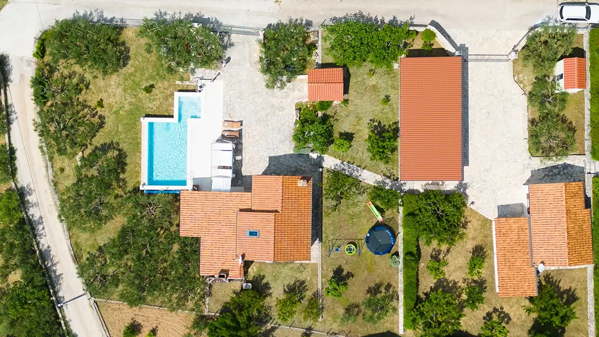 Bird's eye view of the villa and its surroundings, featuring the villa, parking area, pool, children's private outdoor playground, and garden.
